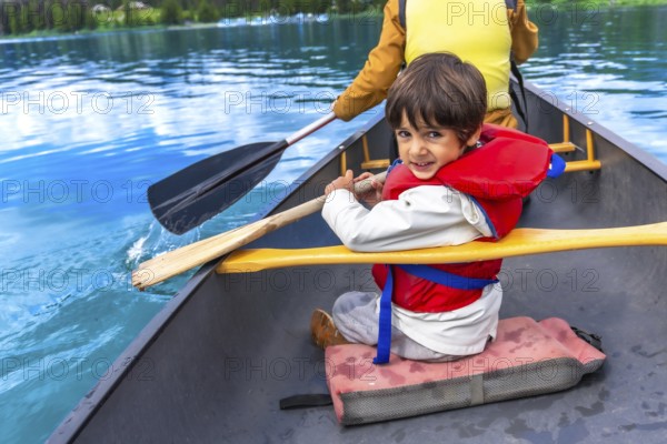 Young boy wearing life jacket paddling canoe on turquoise maligne lake with parent in jasper national park, alberta, canada, enjoying summer vacation together
