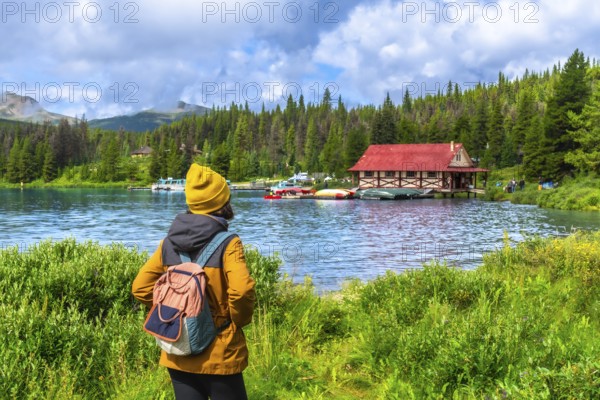 Female tourist wearing a yellow beanie and backpack enjoying the breathtaking view of maligne lake and its iconic red boathouse in jasper national park, alberta