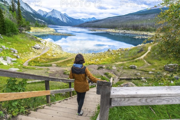 Female hiker descending wooden stairs towards the scenic medicine lake, surrounded by the canadian rockies in jasper national park, alberta, enjoying a peaceful moment in nature during a sunny day