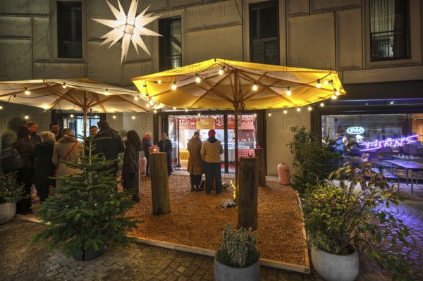Visitors standing outside a café during the evening Advent season, Nuremberg, Middle Franconia, Bavaria, Germany