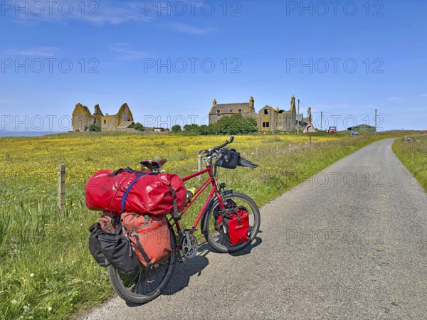 Bicycle with luggage on a dirt road in front of ruins amidst blooming countryside, South Uist, Hebrides, Scotland, Great Britain