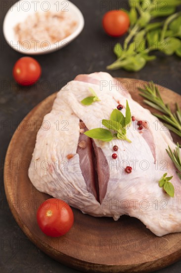 Raw Turkey Thigh with spices and rosemary on cutting board on black concrete background and linen textile. side view, close up, selective focus