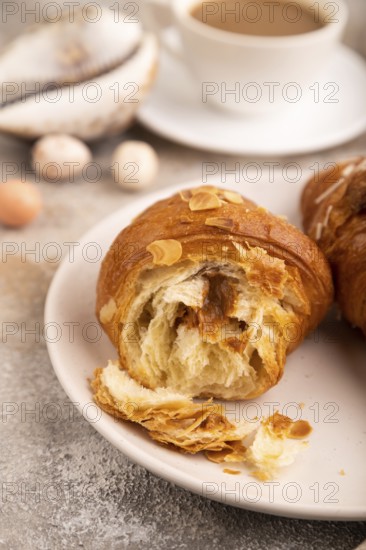 Croissant on white plate on brown concrete background and linen textile, cup of coffee, side view, close up, selective focus
