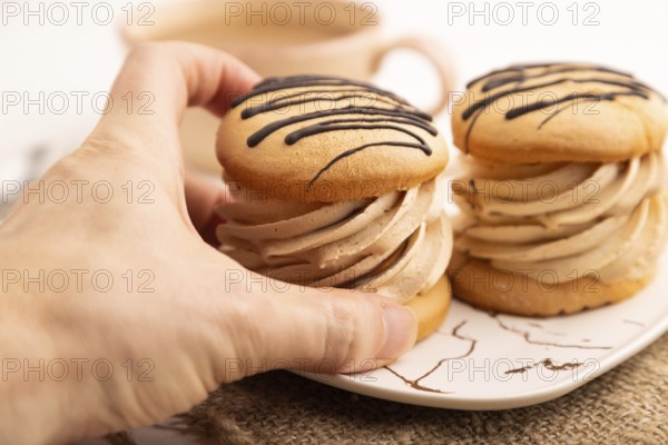 Caramel Cream Cakes with hand on white wooden background and linen textile, cup of coffee, side view, close up, selective focus