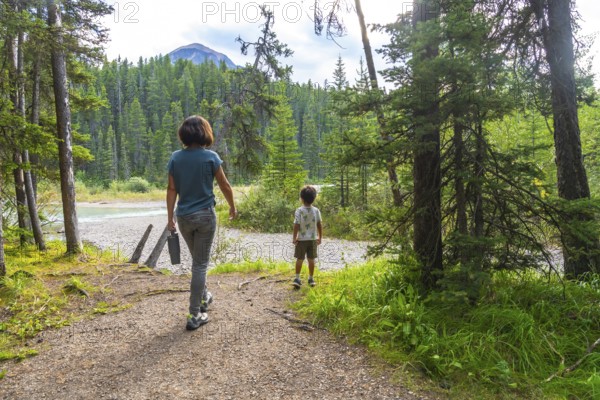 Mother and son enjoying a leisurely hike along a scenic banff national park trail, surrounded by lush greenery, towering evergreens, and a picturesque river