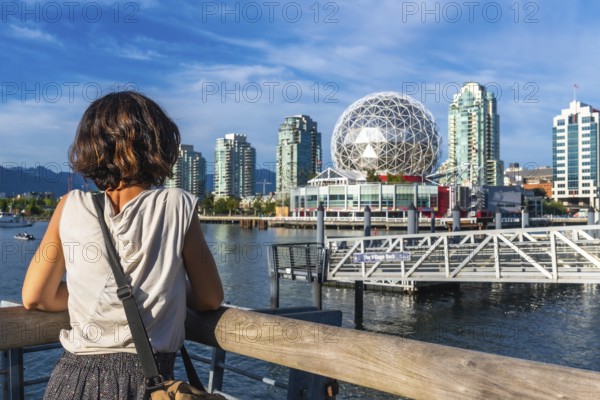 Young woman tourist is enjoying the cityscape of vancouver, british columbia, with science world geodetic dome, modern buildings, and false creek waterfront on a sunny day