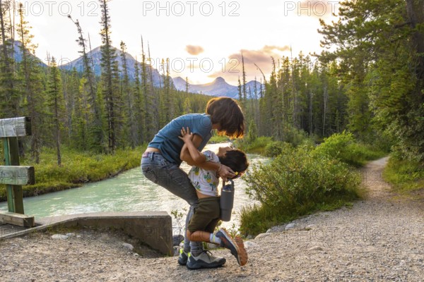 Mother embracing her son by the riverside in banff national park, surrounded by the stunning canadian rockies at sunset, capturing a heartwarming family moment in nature