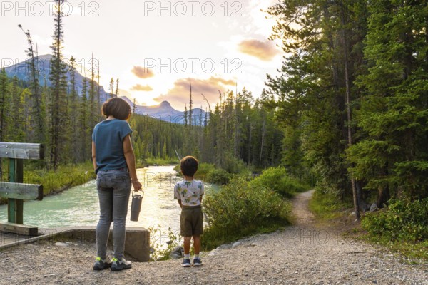 Mother and son enjoying breathtaking sunset view over river and mountains in banff national park, canadian rockies, alberta, canada, during summer vacation