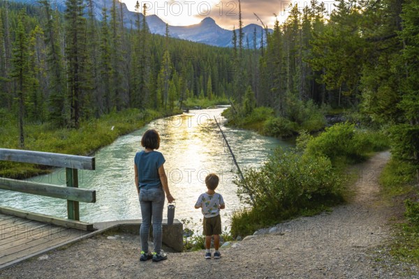 Mother and her son are enjoying a breathtaking sunset view over a pristine river flowing through the lush forests of banff national park, creating a serene moment of connection with nature