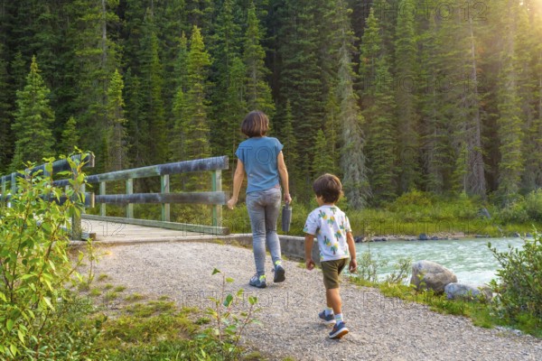 Mother and son enjoying a leisurely hike along a scenic banff national park trail, surrounded by lush forests and a flowing river, capturing a heartwarming family moment in nature