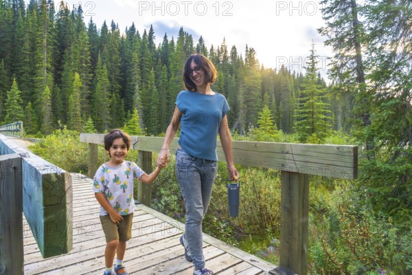 Mother and son holding hands, smiling and walking on a wooden boardwalk surrounded by lush green forest in banff national park, alberta, canada, enjoying quality time in nature