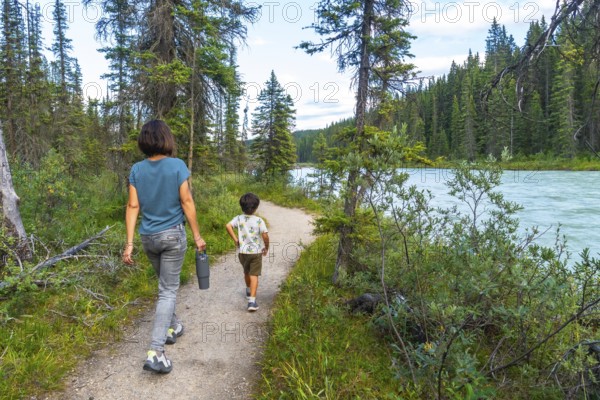 Mother and son enjoying a leisurely hike along a picturesque river in banff national park, surrounded by lush greenery and the majestic canadian rockies