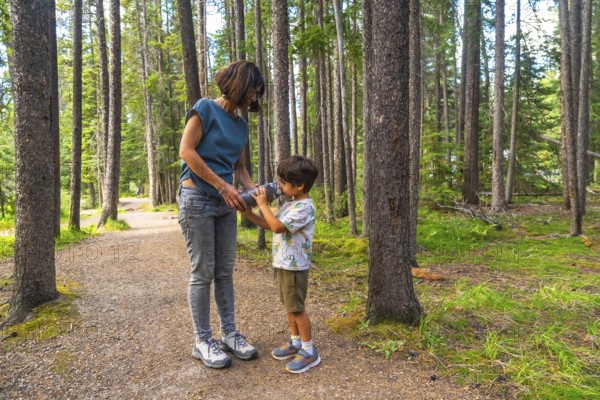 Mother giving a drink of water to her son from a reusable water bottle while hiking on a beautiful summer day in banff national park, canadian rockies