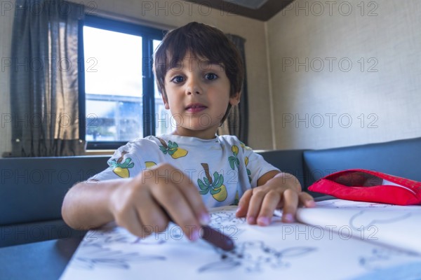 Young boy concentrating on drawing with crayons in a camper van, enjoying creative activities during a family vacation in banff national park, canadian rockies