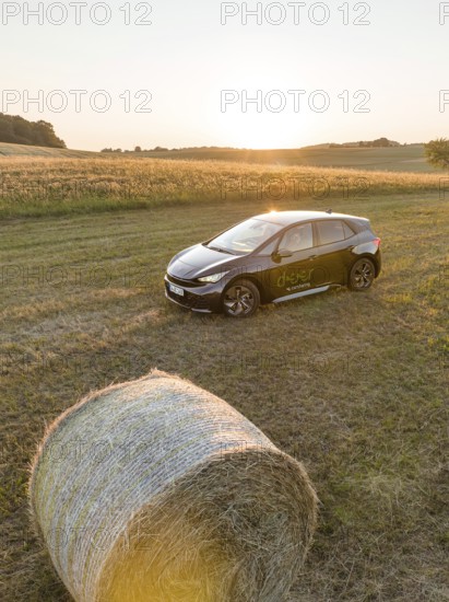 A black car is parked in a field next to a hay bale at sunset, deer e-car sharing, Cupra electric car, Black Forest, Germany