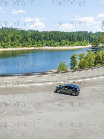A car on a winding track with a view of a lake and forest in the background, deer e-car sharing, Cupra electric car, Germany