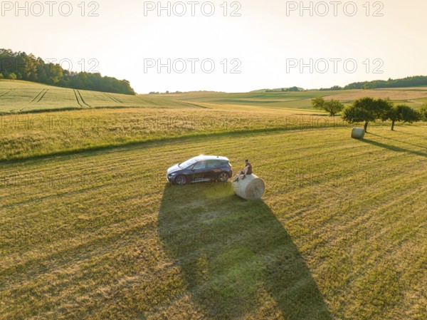 Car next to a hay bale in the middle of a vast golden field under the evening sun, deer e-car sharing, Cupra electric car, Gechingen, Germany