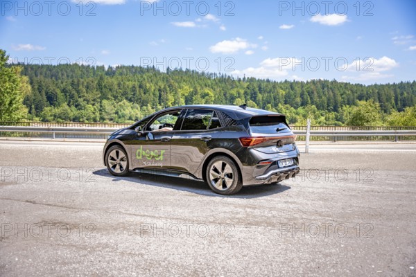 Black car on a country road against a background of green forest and blue sky, deer e-car sharing, Cupra electric car, Germany