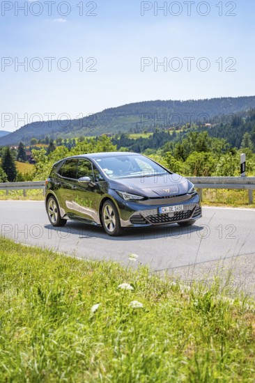 Black car driving on a road through a hilly landscape in daylight, deer e-car sharing, Cupra electric car, Germany
