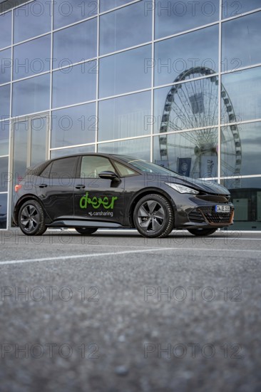 Black car in front of a modern building with glass façade, Ferris wheel reflected in the windows, deer e-car sharing, Cupra electric car, Böblingen, Germany