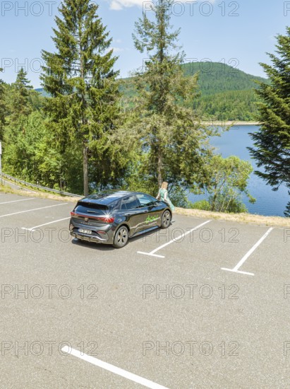 A car is parked in a parking lot with a view of a lake and surrounded by forest and mountains, deer e-car sharing, Cupra electric car, Black Forest, Germany