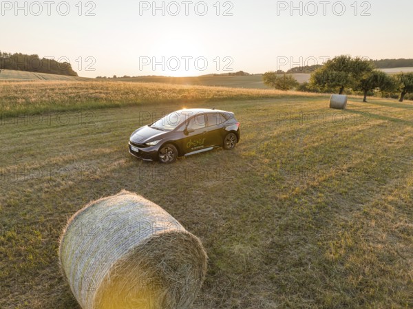 A car is parked in a field with hay bales at sunset, surrounded by meadows, deer e-car sharing, Cupra electric car, Black Forest, Germany