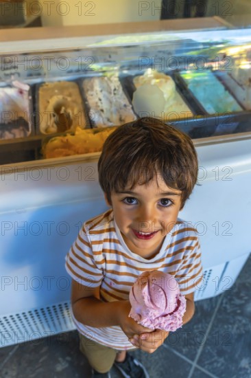 Smiling child holding a strawberry ice cream cone in front of a display case full of colorful ice cream flavors in vancouver, british columbia
