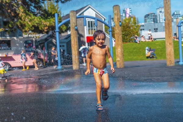 Happy child is running through water jets at a playground in vancouver, british columbia, on a sunny summer day, enjoying the refreshing spray and creating a rainbow effect