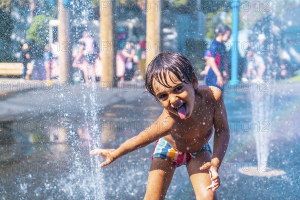 Happy child sticking out his tongue while playing in a water fountain on a sunny day in vancouver, british columbia, enjoying a playful moment of summer refreshment