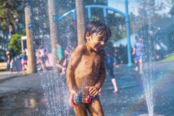 Happy muddy child playing and enjoying a refreshing spray in a water fountain at a playground in vancouver, british columbia, on a sunny summer day