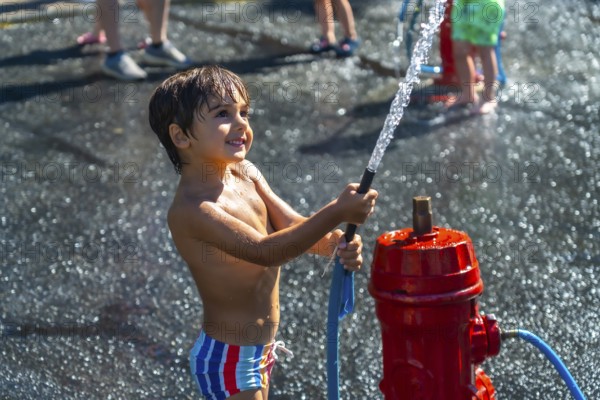 Smiling boy spraying water from a fire hydrant during a hot summer day in vancouver, british columbia, enjoying outdoor play and refreshment