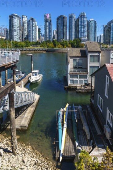 Kayaks resting on a wooden dock near floating homes, with a motorboat moored nearby and the vancouver skyline in the background, create a peaceful and scenic urban waterfront view