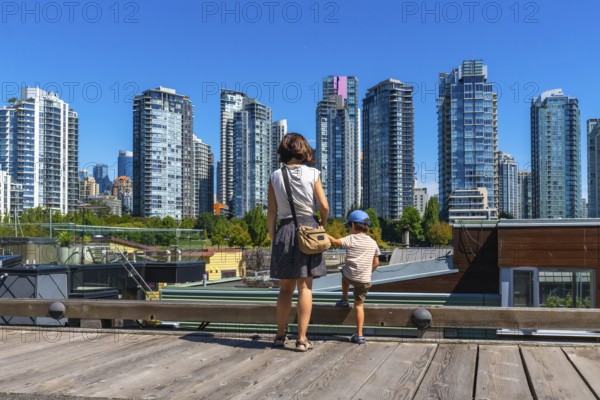 Mother and her son are enjoying the breathtaking view of the vancouver skyline, with its modern skyscrapers and vibrant cityscape, from the wooden deck of granville island market on a sunny day
