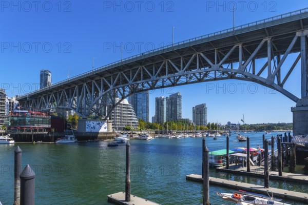 Granville street bridge dominating the vancouver skyline, connecting downtown to granville island across false creek, with boats navigating the waters and modern buildings rising in the background