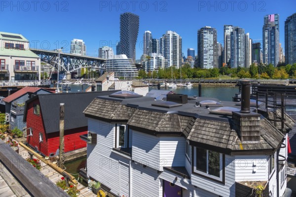 Colorful floating homes contrasting with vancouver's high rise skyline under a clear blue sky, highlighting the unique urban landscape of granville island, british columbia