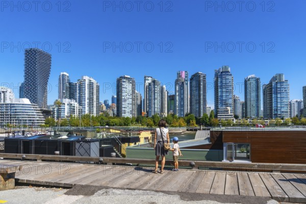 Mother and son standing on a wooden pier, admiring vancouver's modern skyline with high rise buildings and a clear blue sky from granville island market