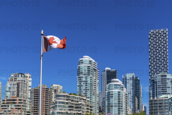 Canadian flag waving proudly in the foreground with the modern skyline of vancouver, british columbia, in the background on a sunny day with clear blue sky