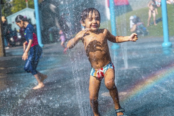 Happy child running through jets of water in a playful splash park on a hot summer day in vancouver, british columbia, enjoying the refreshing spray and creating a rainbow
