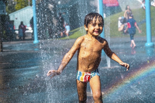 Happy muddy child playing and running through jets of water in a playground water park fountain in vancouver, british columbia, canada, enjoying summer vacation