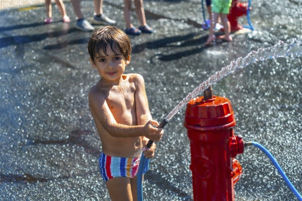 Happy child playing with water jet from a red fire hydrant during a hot summer day in vancouver, british columbia, canada, enjoying a playful moment of refreshment and fun