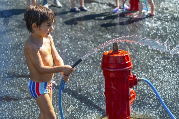 Happy child spraying water with a fire hydrant during a hot summer day in vancouver, british columbia, enjoying outdoor activity and having fun with friends in the background