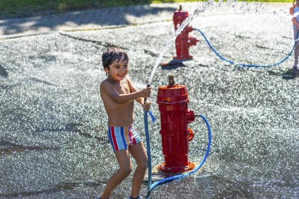 Happy child playing and splashing with water jets coming out of a small red fire hydrant during a hot summer day in vancouver, british columbia