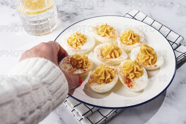 Stuffed eggs with paprika, on a plate, a woman's hand reaches for it