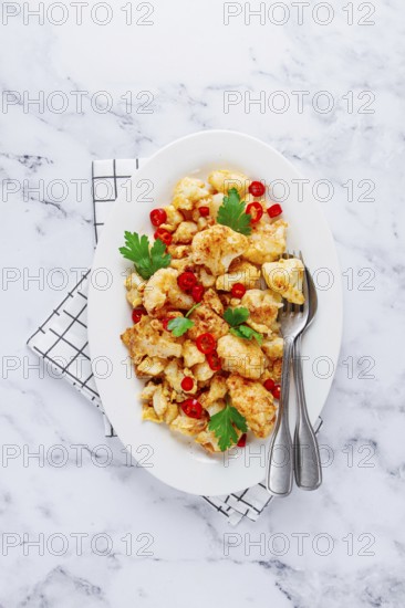 Cauliflower dish, with chili pepper and parsley, on a white plate served on a marble countertop