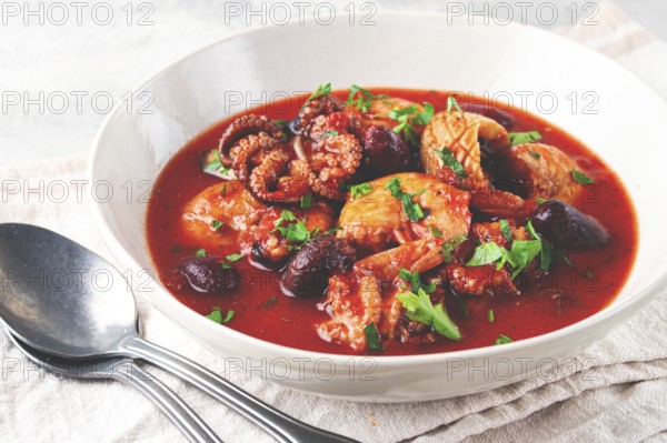 Seafood assortment in tomato sauce, olives, in a white plate
