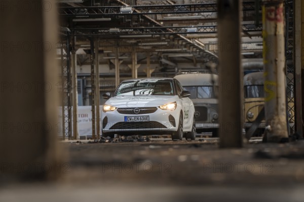 A white Opel with car sharing logo stands between other vehicles in an old industrial building, Deer E-Car Sharing, Motorworld Rüsselsheim, Germany