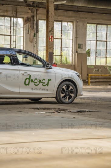 A white car with car sharing logo is parked in a hall with large windows, Deer E-Car Sharing, Motorworld Rüsselsheim, Germany