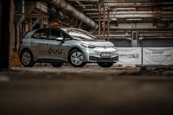 An electric vehicle is parked in an empty, urban factory building with visible pipes and structures, Deer E-Car Sharing, Motorworld Rüsselsheim, Germany