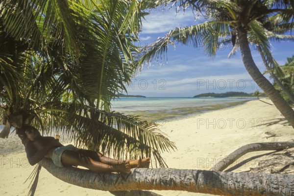 Boy lying on a coconut tree on the beach of Tavewa Island, Yasawa Islands, Fiji