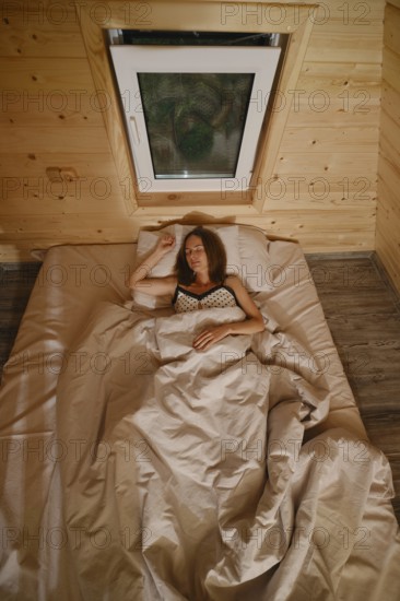 A woman sleeping in bed in a wooden room covered with blanket